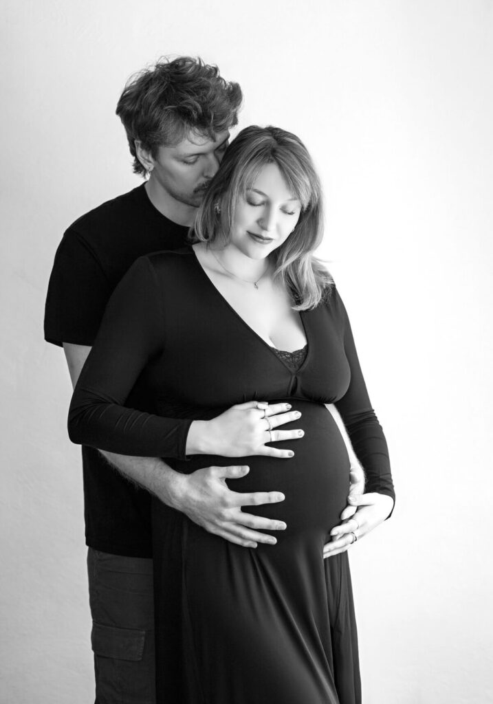 Black-and-white maternity portrait of a couple embracing, with the man tenderly holding the woman's pregnant belly, showing their journey of overcoming photoshoot fears.